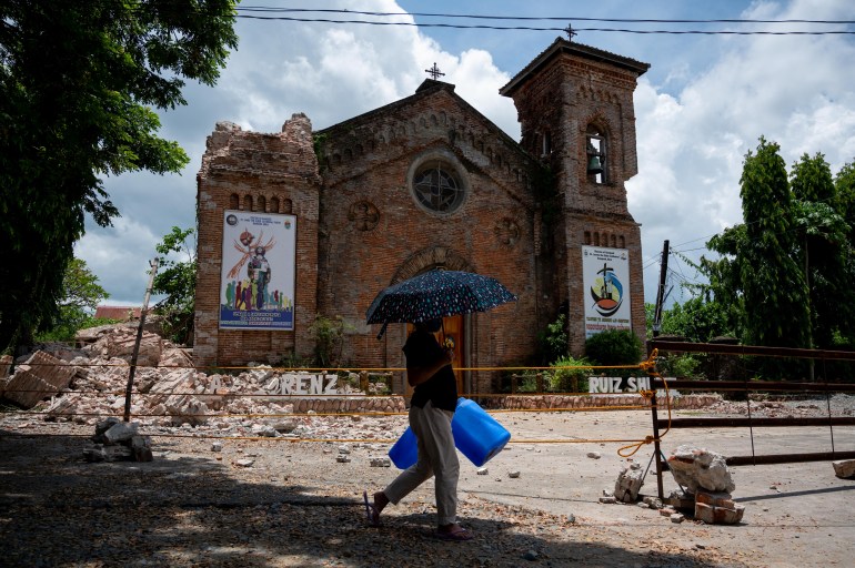A woman walks past a damaged church in the aftermath of an earthquake in Bangued, Abra province, Philippines in July 2022 [File: Lisa Marie David/Reuters]