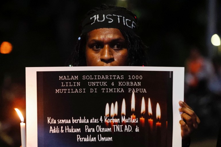 A demonstrator holds a sign and a candle during a protest to ask for justice following the mutilation of four civilians in Timika, Papua