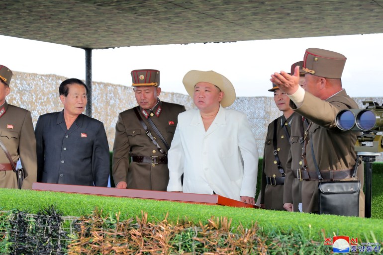 Kim Jong Un in white jacket and straw hat with his military commanders watching a missile launch.