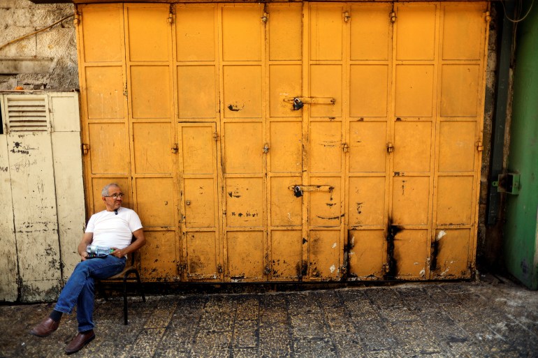A man sits outside of a shop which is closed 