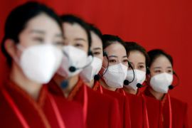 a group of women in red cheongsams and white face masks line up against a red wall at an exhibition in conjunction with the 20th party congress