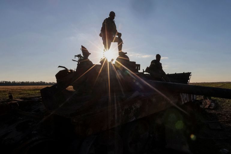 Ukrainian soldiers stand on top of a destroyed Russian tank silhouetted against the sky