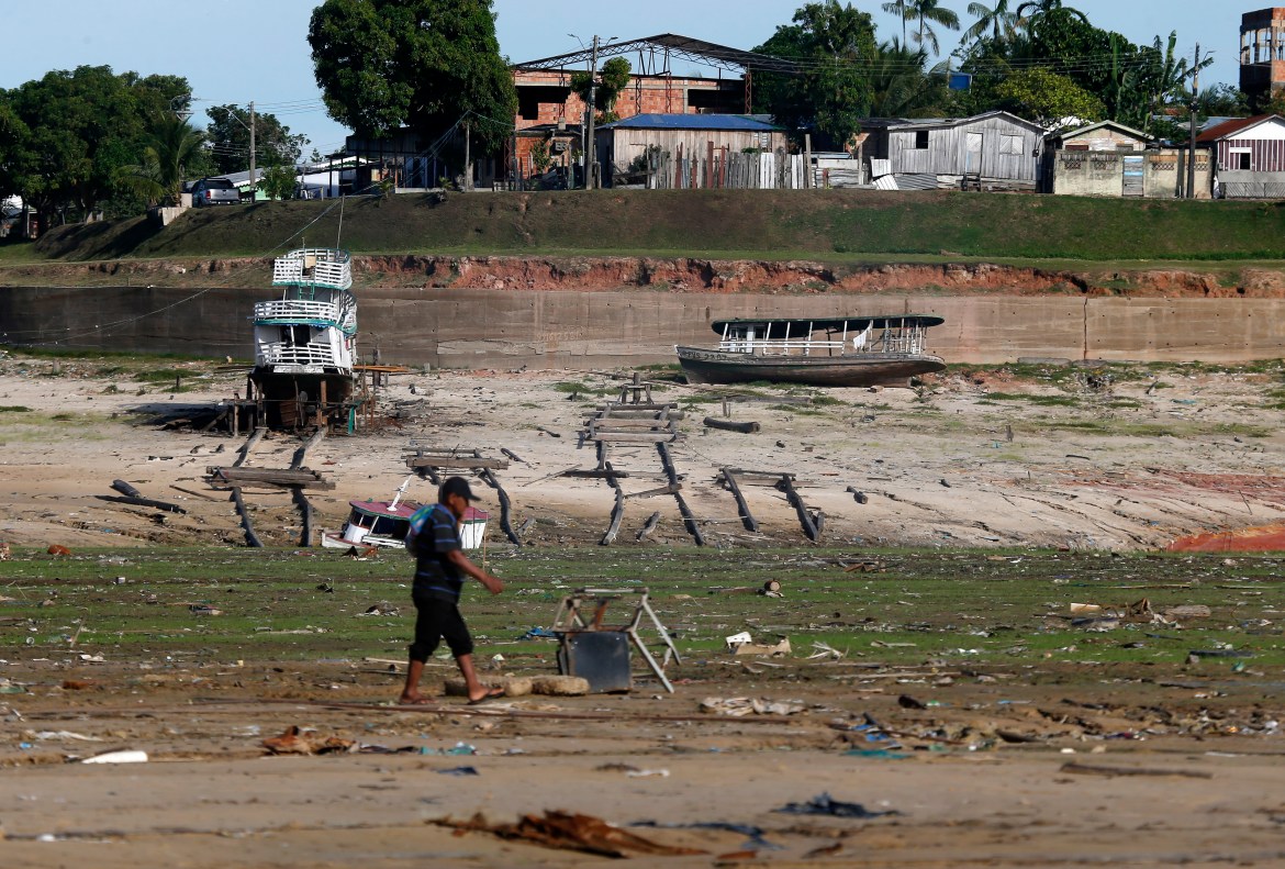 A man walks by boats on dry land in an area impacted by the drought near the Solimões River, in Tefe, Amazonas state, Brazil