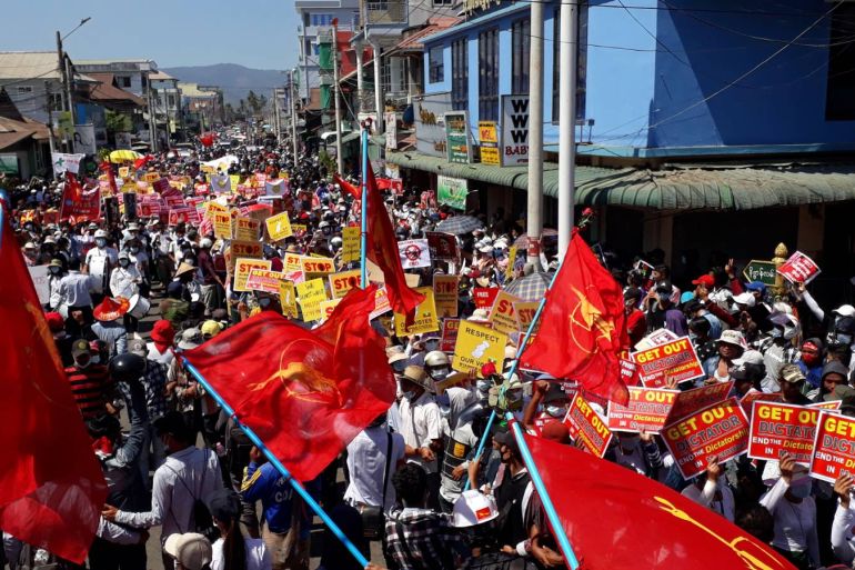 Crowds of people march through a street in Launglone in September with red flags and placards reading 'Get out dictator. End the dictatorship in Myanmar'.