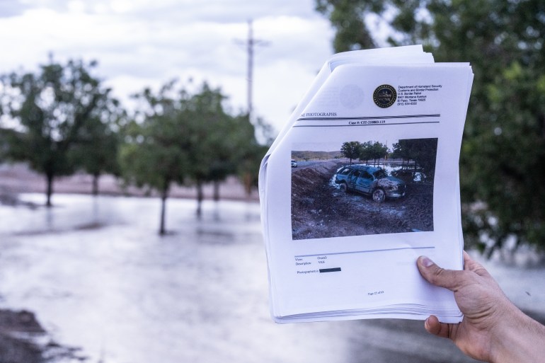 A photo of someone holding several pieces of paper folded on a photo of a car on water on the piece of paper with a flooded field and trees in the background.