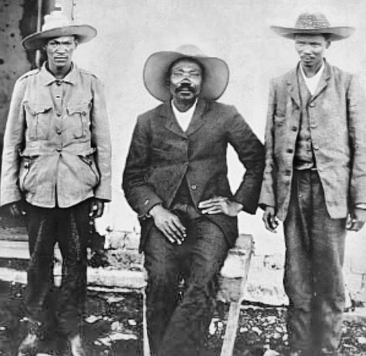 A photo of Jacob Morenga (centre), leader of African partisans with two other men standing on either side of him.