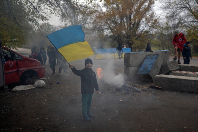 A boy flies a Ukrainian flag at a former Russian checkpoint on the outskirts of Kherson