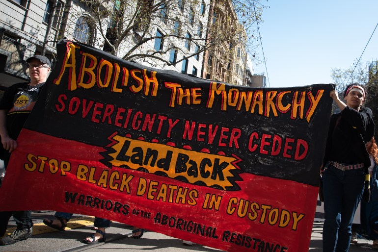 Protesters in Melbourne march with a giant banner in the colours of the Aboriginal flag reading 'Abolish the monarchy, sovereignty never ceded, land back, stop black deaths in custody'