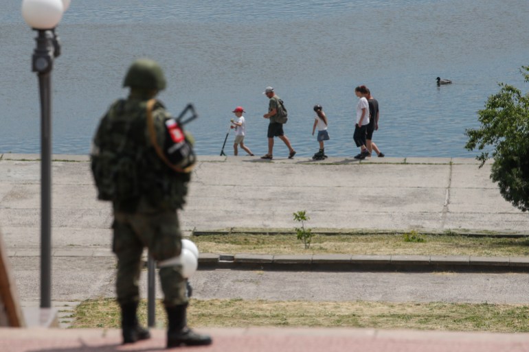 A picture taken during a media tour organized by the Russian Army shows a Russian serviceman standing guard as a family walks on a promenade along the Dnipro River in Kherson, Ukraine