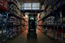Forklift drives along aisle in between stocked factory shelves