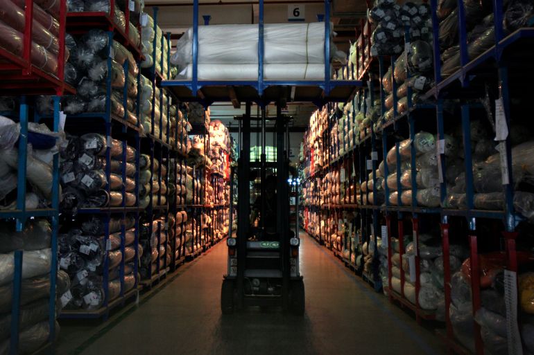 Forklift drives along aisle in between stocked factory shelves