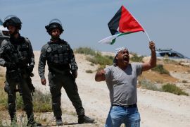 A man waving a Palestinian flag next to two Israeli soldiers