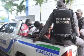 Dominican police ride with detained Haitian nationals in the flatbed of a truck