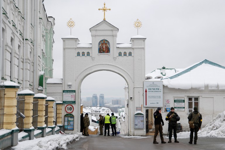A group of Ukrainian law enforcement officers standing at the entrance to the Kyiv Pechersk Lavra monastery compound. There is snow on the ground and on rooftops..