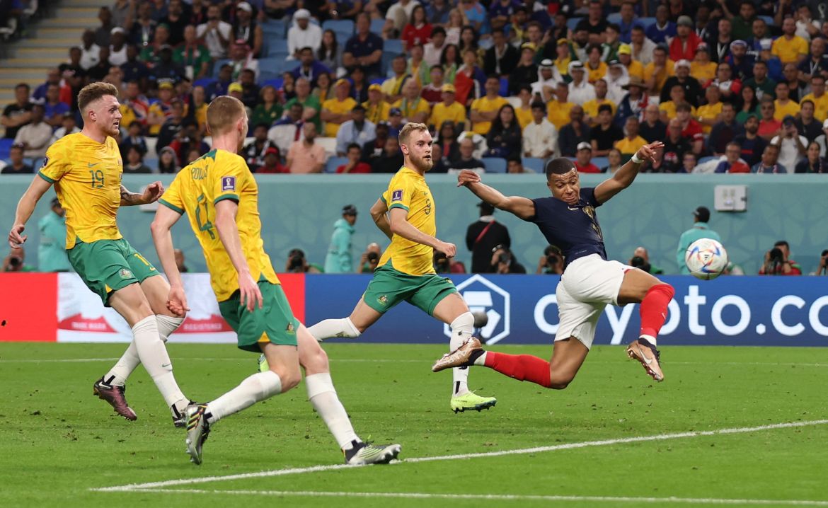 Mbappe in mid-air, his body twisted, as three Australian players run behind him