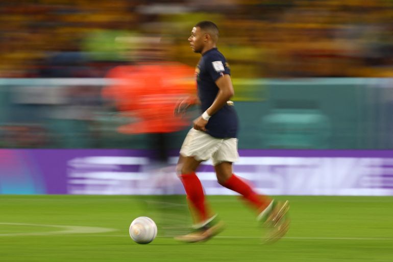 A motion blurred picture of Mbappe from the side as he moves across the field kicking a ball