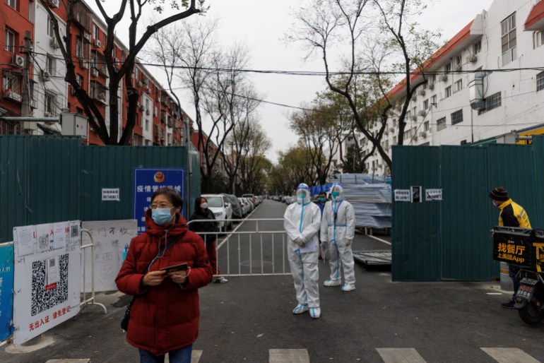 Two workers in white hazmat suits stand guard outside a Beijing apartment block that is surrounded by barriers.