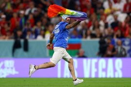 A pitch invader runs onto the field wearing a t-shirt with a message saying 'Respect for Iranian Women' while holding a rainbow flag.