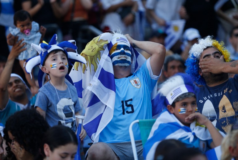 Uruguay fans react in disbelief and disappointment, grasping their head or putting a hand to their mouth.