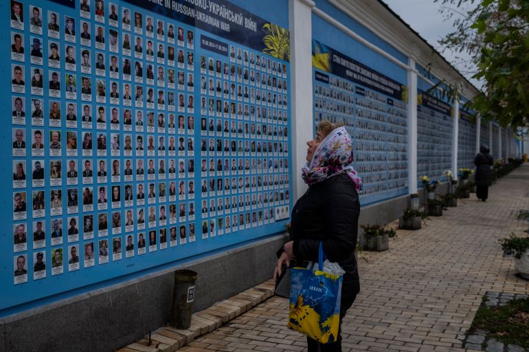 A woman stands in front of the 'memory wall of fallen defenders' in downtown Kyiv