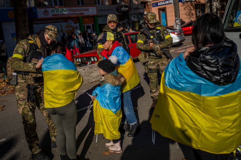 Ukrainians with flags draped around their shoulders ask Ukrainian solider to sign them after the liberation of Kherson