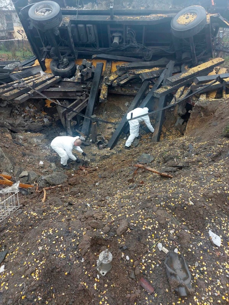 Investigators in hazmat suits sift through the crater created by a missile that fell on a Polish village. A truck overturned in the blast is behind them