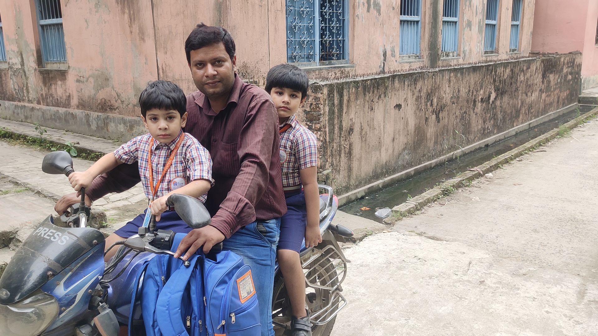 A photo of Arijit Khan with his two children, one in front and one behind him on a motorcycle.
