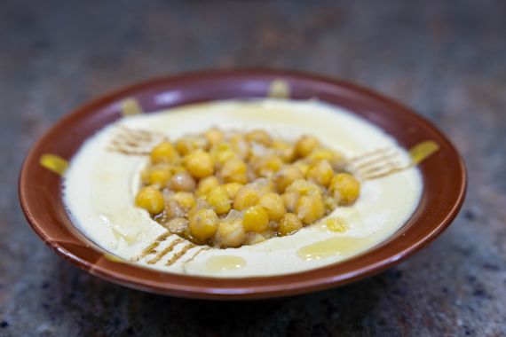 A brown bowl with hummus arranged in it, and a scoop of golden chickpeas in the middle