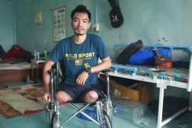 Salai Peter, who had both legs amputated at the knee, in a blue 'Polo Sport' T shirt and shorts sitting in a wheelchair at the rehabilitation centre with beds and a guitar behind him.