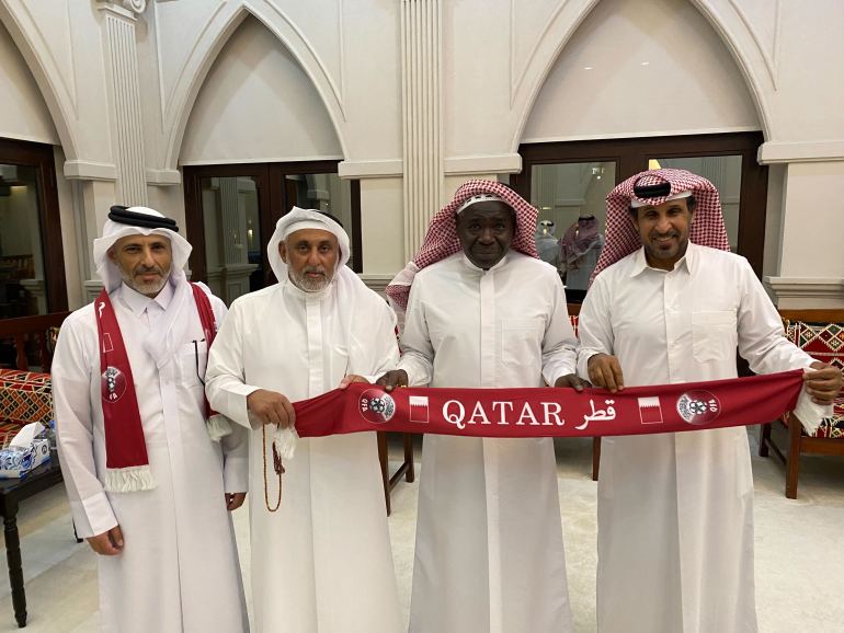 Four guests at a traditional Qatari majlis, gathered to watch the opening ceremony of the football tournament, hold a Qatar banner.