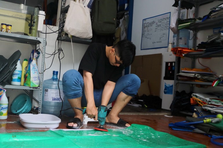 A worker washes discarded plastic at the Dong Dong Saigon workshop. He is sitting on a very low stool and wearing protective glasses