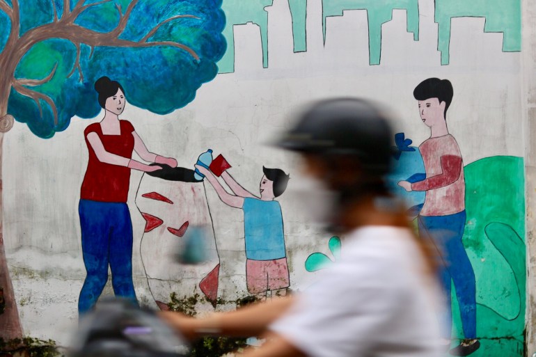 A mural in Ho Chi Ming City showing a woman holding a rubbish bag and a boy putting rubbish inside and another man bringing rubbish. A motorcycle rider is passing the mural and is blurred.