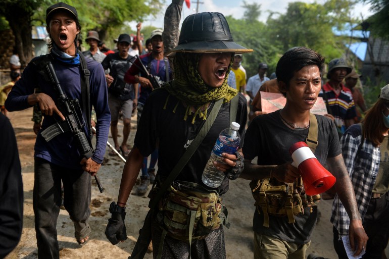 Anti-coup fighters and protesters at a rally in Myanmar's Sagaing region. They are shouting as they walk. Some have weapons and one is carrying a megaphone.