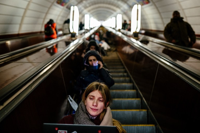 A woman sitting on the stopped escalator of a Kyiv metro station after an air raid warning. Other residents are also sheltering there.