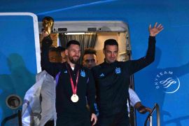 Argentina's captain and forward Lionel Messi (L) holds the FIFA World Cup Trophy alongside Argentina's coach Lionel Scaloni