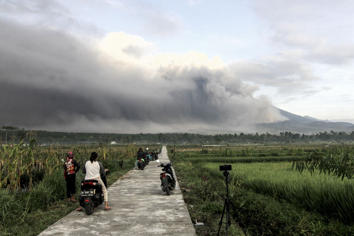 Mount Semeru spews volcanic materials to the air as people look on