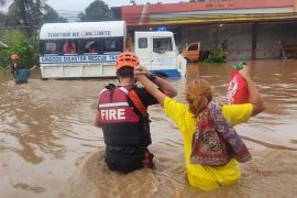 A fire rescue worker is holding a resident's hand as they walk through a flooded street with water up to their waist on Christmas day in Gingoog city, Misamis Oriental province, Philippines.