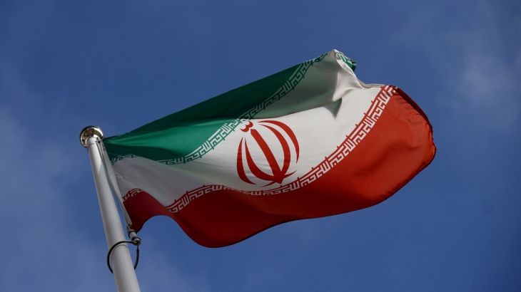 The Iranian flag flying on a pole against a blue sky.