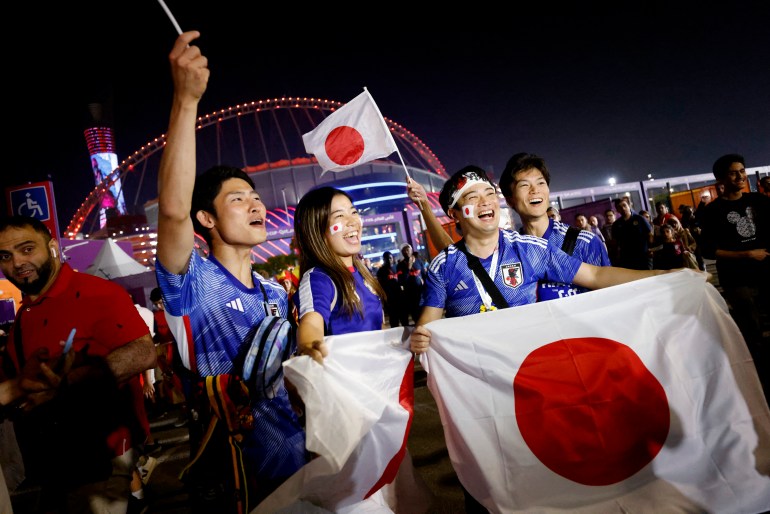 Fans holding up a Japanese flag and wearing their team's colours