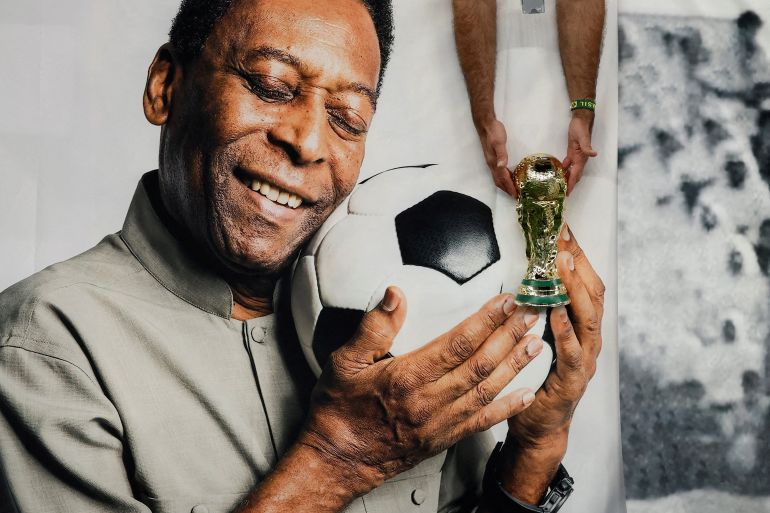 A Brazil fan holds a replica World Cup trophy in front of a banner of legendary Brazilian player Pele before the Cameroon vs Brazil match at Lusail Stadium, Lusail, Qatar