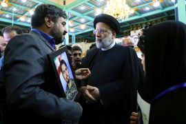 A man on the left holds a framed picture of a man in his hands while talking to Iran's President Raisi, who is standing on the right.