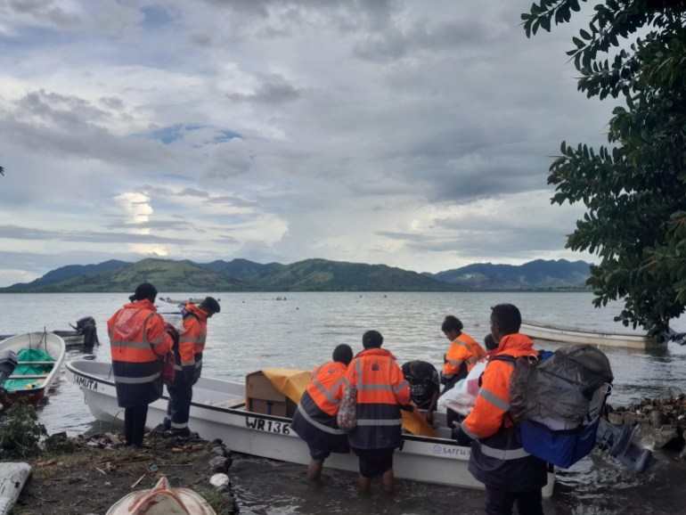 A group of election observers getting in a boat on an island in Fiji. The sky is cloudy and they are wearing lifejackets