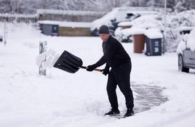 A man clears snow as cold weather continues in Hertford, Britain