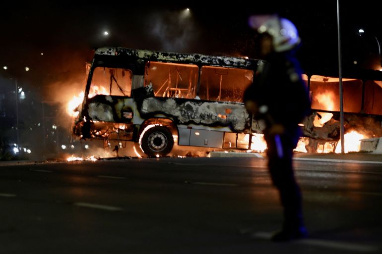 A police officer stands near a burning bus
