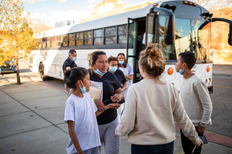 A family talk to shelter workers in front of a bus.
