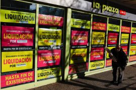 A customer exits a supermarket in Madrid with posters announcing closing down sales