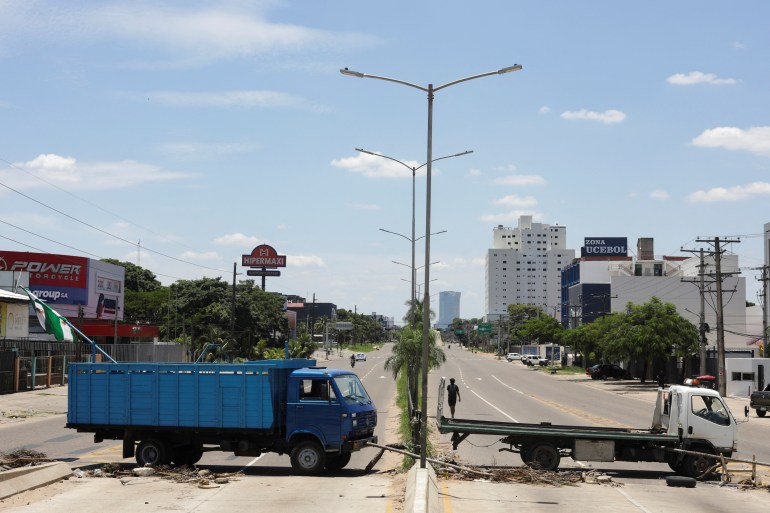 Two trucks, one big blue one and another in front of it, block a road each. There is one man walking down the road behind a truck