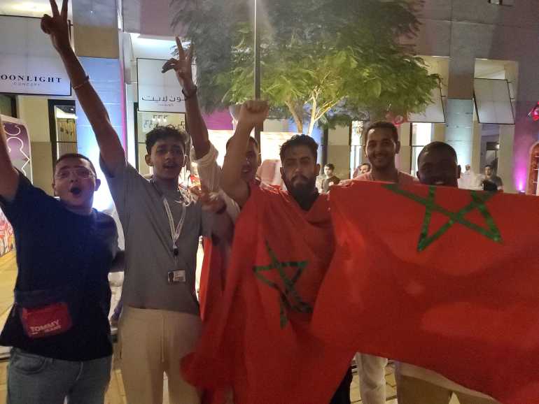 Young men hold up Moroccan flag and their arms in celebration