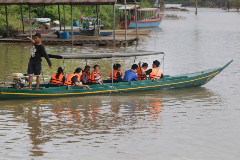 A boat filled with tourists set off onto the Mekong in the hope of catching a glimpse of the Mekong dolphin. The people are wearing life jackets and the boat is uncovered. There are other boats moored along the bank behind them