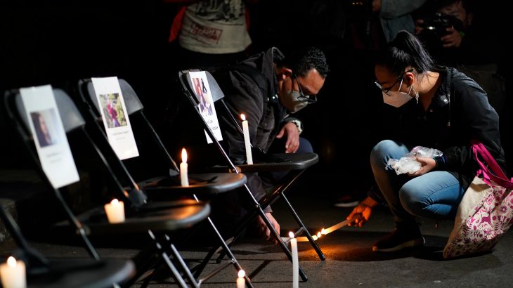 A couple lights a candle next to a vigil for slain journalists, with pictures taped to empty chairs